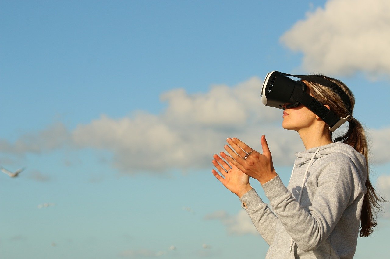 Woman wearing an AR/VR headset amid a blue sky filled with clouds.